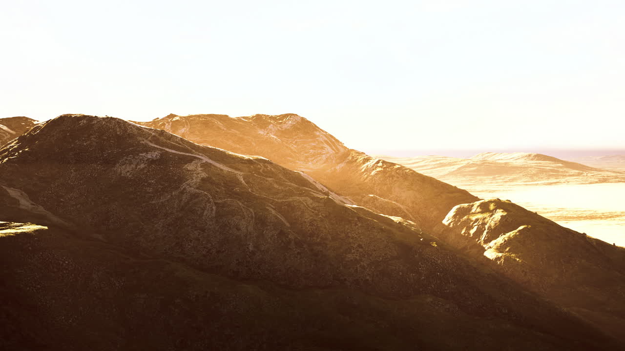Golden sunlight illuminates the rugged mountains at sunset by the coast