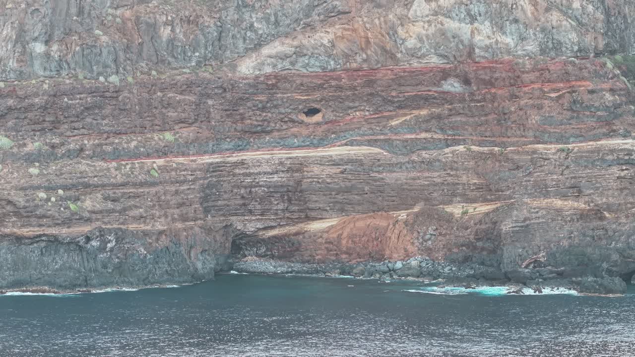 Drone view of steep coastal cliffs with red and gray historic geological rock layers, Tenerife, Canary Islands, Spain