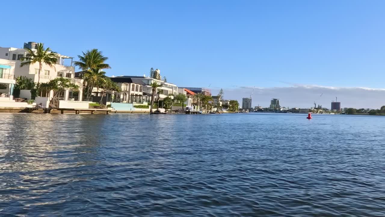 Explore luxurious waterfront homes with a backdrop of city skyscrapers under a clear blue sky.