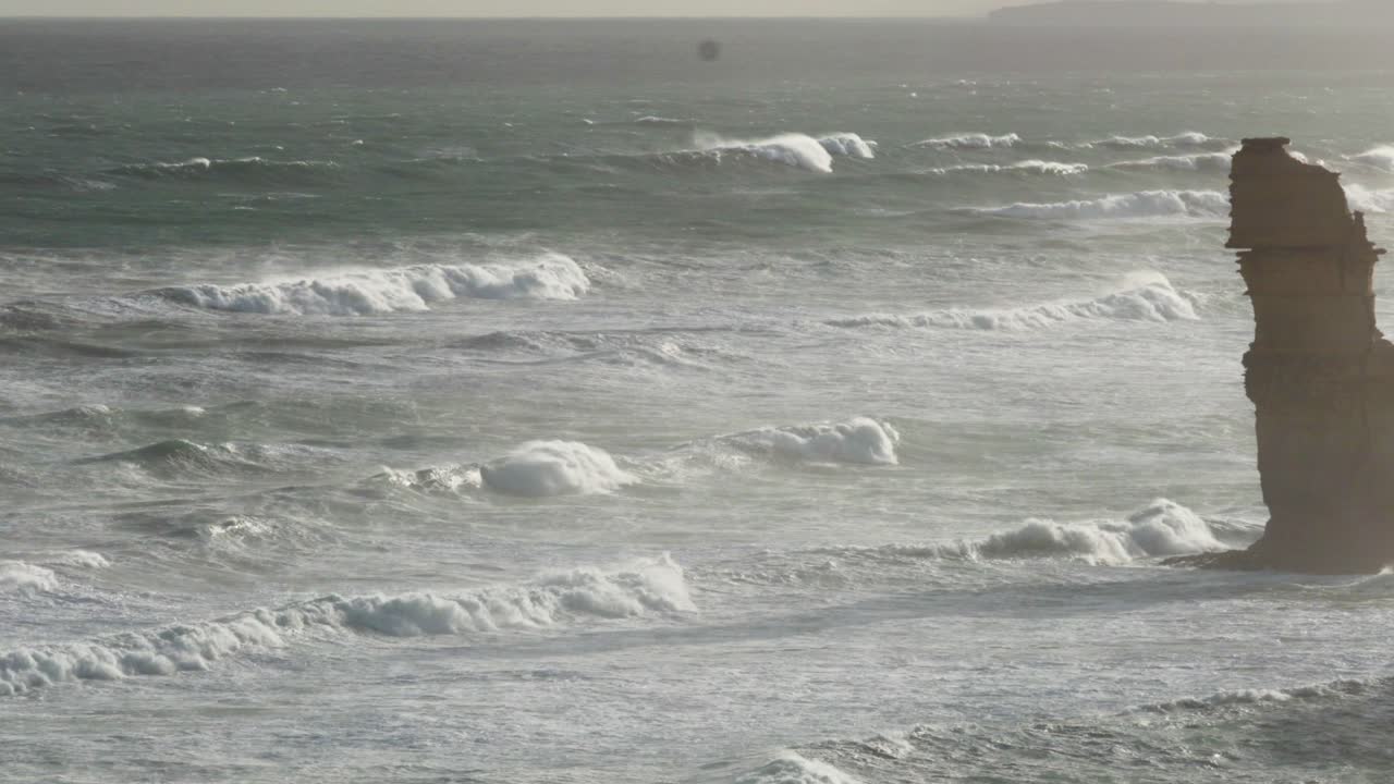 Dynamic ocean waves crash against the iconic limestone stacks of the Twelve Apostles, captured in serene natural lighting