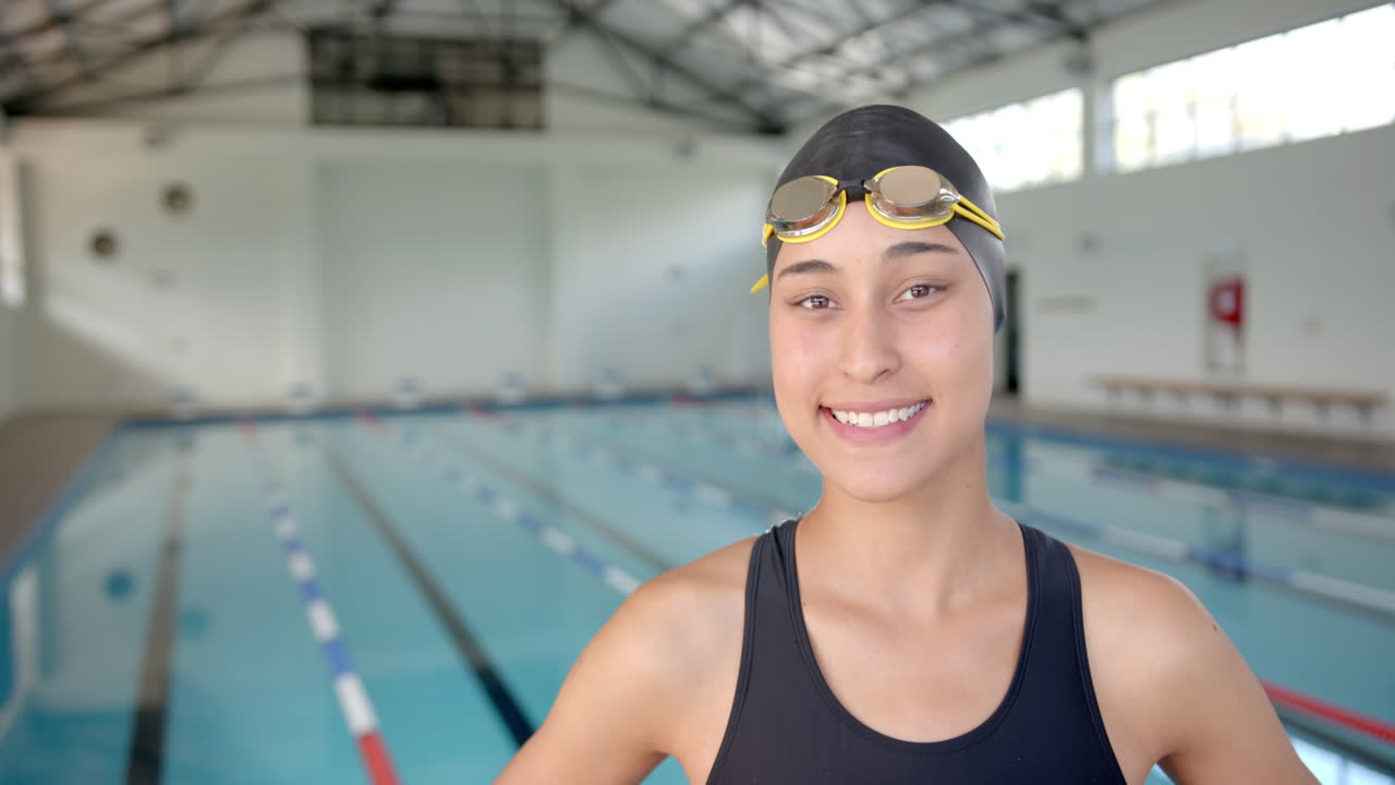 Smiling Female Swimmer wearing goggles standing by indoor swimming pool, ready to train