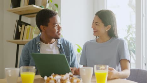 Couple enjoying breakfast and using a tablet at home