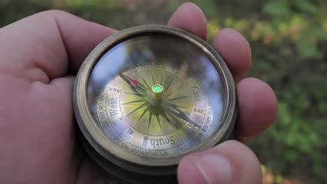 Traveler-hand-holds-a-old-directional-compass-in-summer-forest.-Person-use-compass-to-find-location.-Travel-concept-close-up.