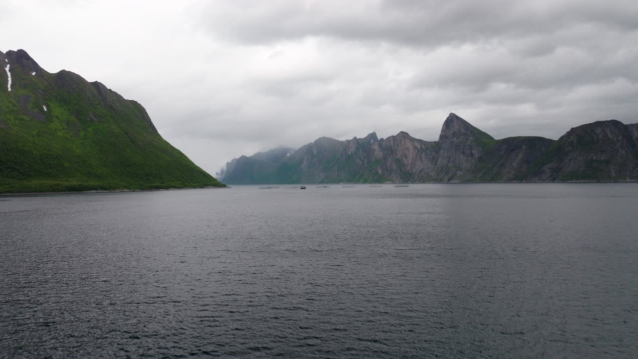 Vasche di allevamento ittico per acquacoltura con montagne imponenti in una giornata nuvolosa a Senja, Norvegia. Avvicinamento aereo, spazio per il testo.
