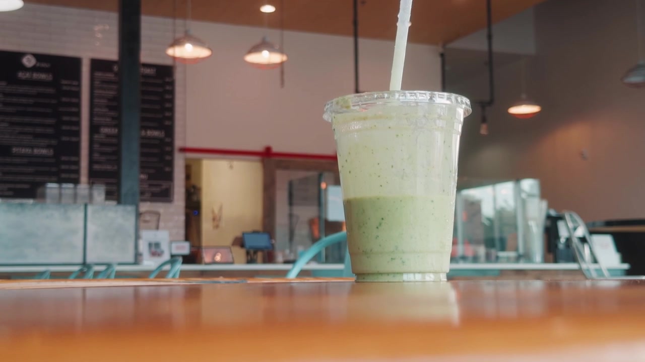 Camera rises above a table edge to reveal a green smoothie in a cafe.