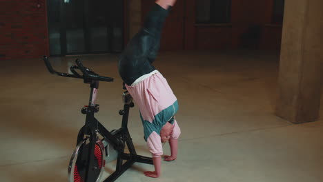 Athletic-girl-make-acrobatic-trick-on-bike-exercising-workout-on-stationary-cycling-machine-indoors