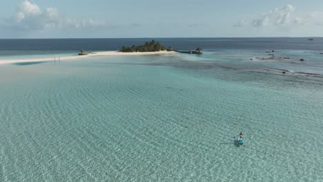 isla tropical remota con una mujer paddleboarding en aguas poco profundas, aéreo