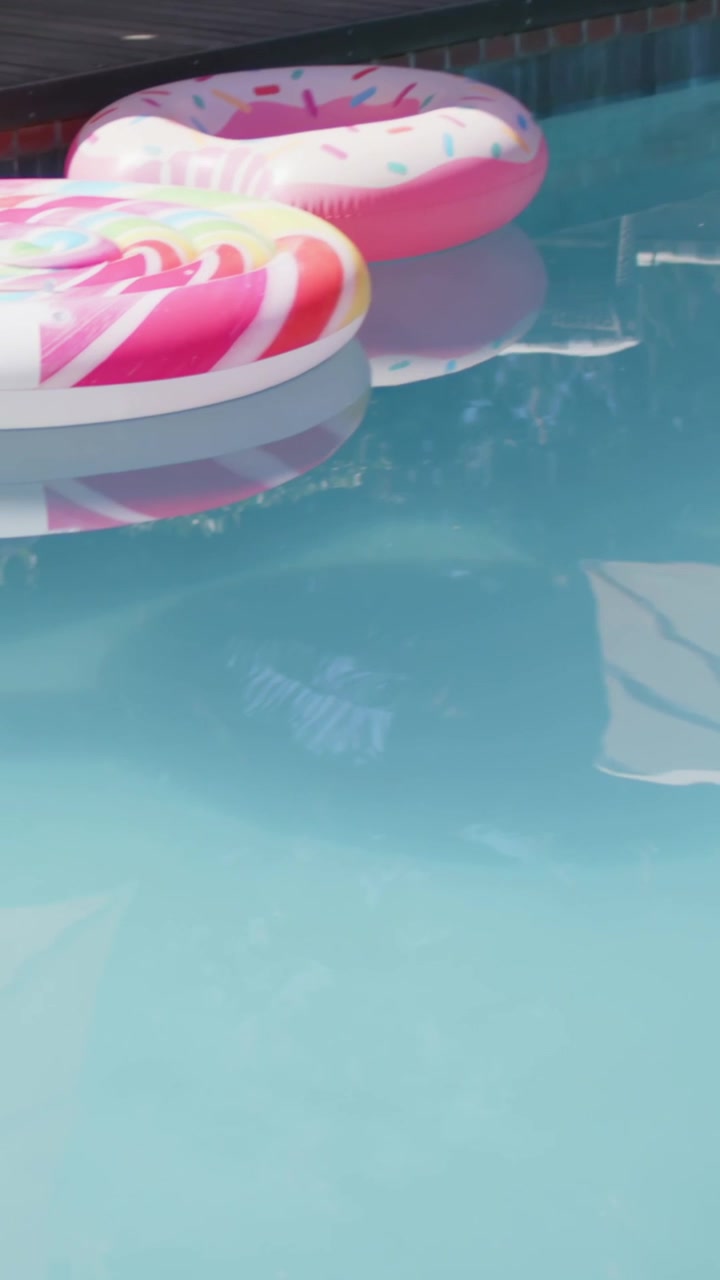 Vertical video: Camera panning, colorful donut floats drifting at pool edge for leisure shot