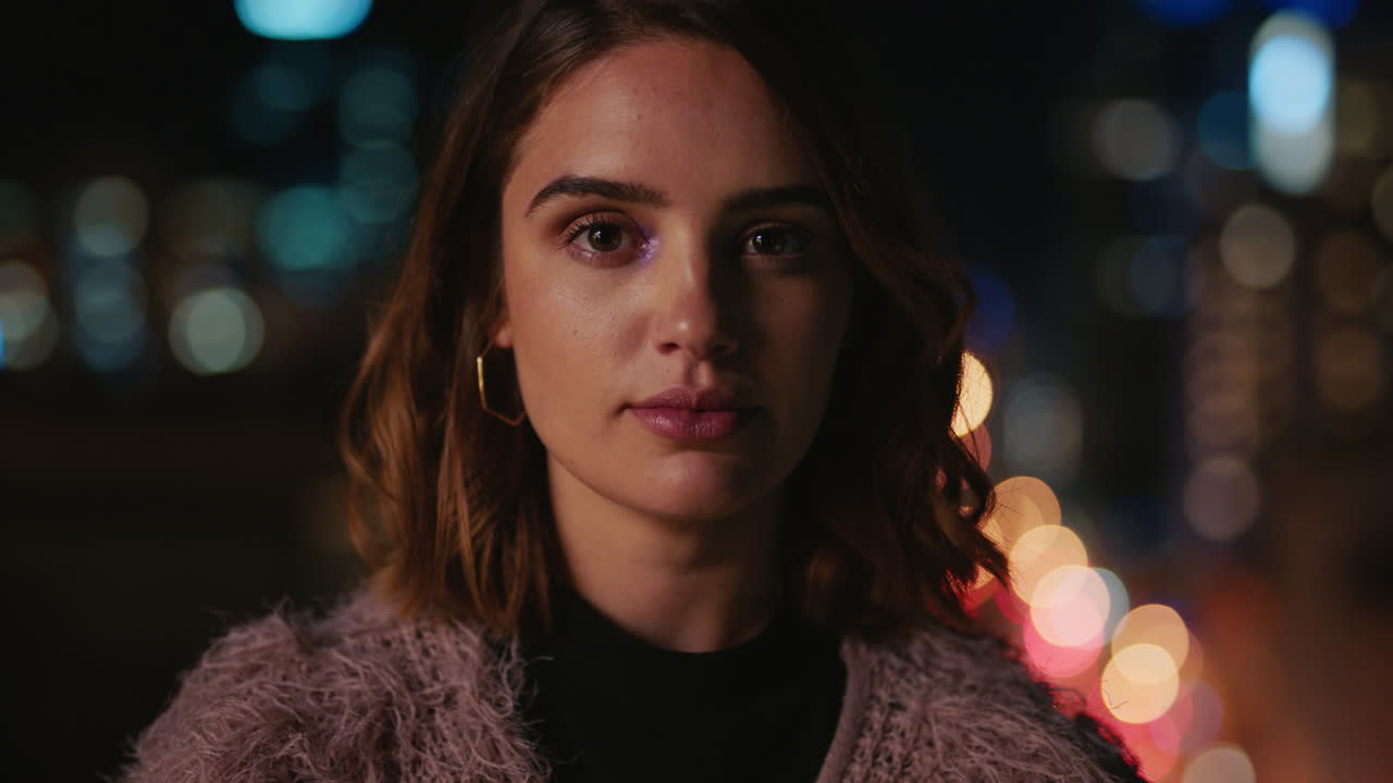 밤에 지붕 위에 있는 아름다운 젊은 백인 여성의 초상화. 도시 스카이라인 배경에 보케 도시 불빛이 있습니다.