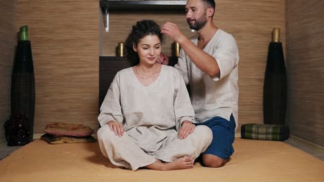 attractive thai massagist is massaging young woman's head standing behind her