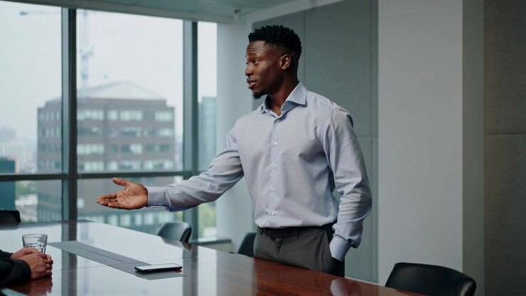 Presenting man in blue shirt facing peer, gesturing, explaining plan in office, phone, copy space