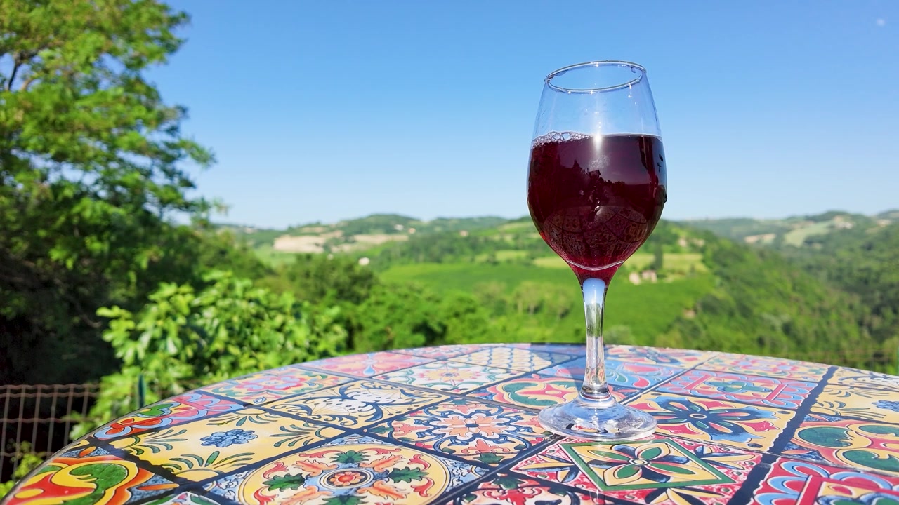Versare vino rosso in un bicchiere su un tavolo colorato con vista panoramica sulle colline