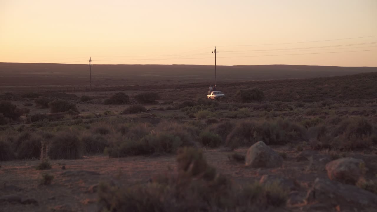 A pickup truck with farm laborers travels along a dusty road in a semiarid desert at sunset