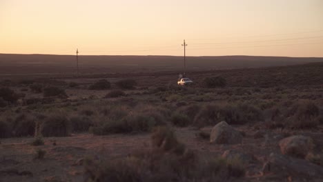 a pickup truck with farm laborers travels along a dusty road in a semiarid desert at sunset