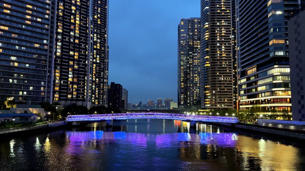 paisaje urbano al anochecer con edificios de gran altura y un puente iluminado que se refleja en el río