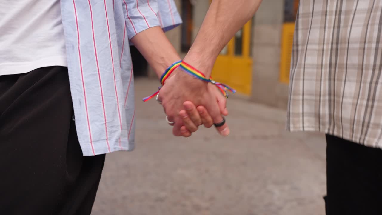 Coppia LGBTQ+ che si tiene per mano con braccialetti arcobaleno per strada