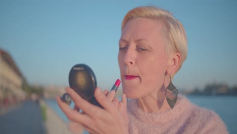 Portrait-of-Older-Adult-Female-With-Short-Blonde-Hair-Fixing-Lipstick,-Close-Up-Slow-Motion