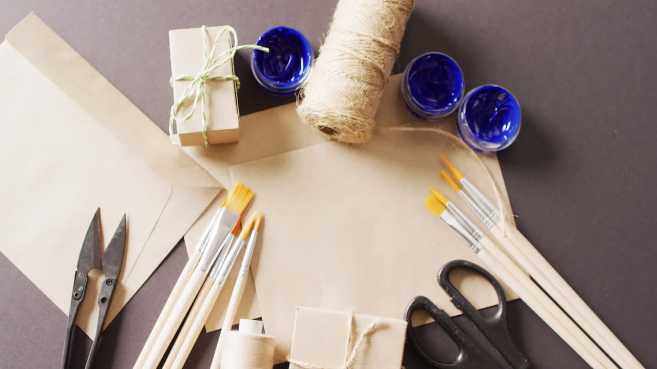 vídeo de paquetes con cuerda, tarjeta, tijeras, pinceles y pintura sobre fondo gris