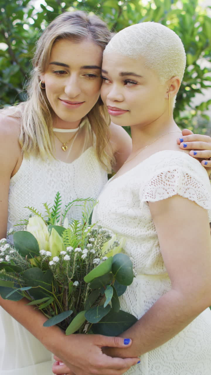 정원에서 포옹하는 꽃 어리와 함께 행복한 다양한 여성 커플의 수직 비디오