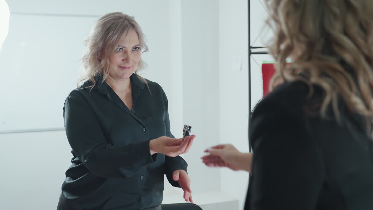 close up saleslady rises to present key near detailed building miniature as client stretches forth hand to receive key and they exchange handshake with warm demeanor beside pen holder on office table