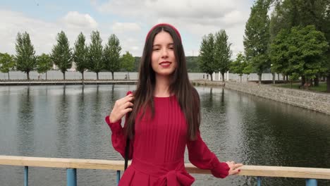 hermosa chica en sonrisas rojas en el puente junto al lago