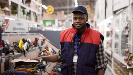 smiling salesman standing between rows in hardware store, looking to the camera