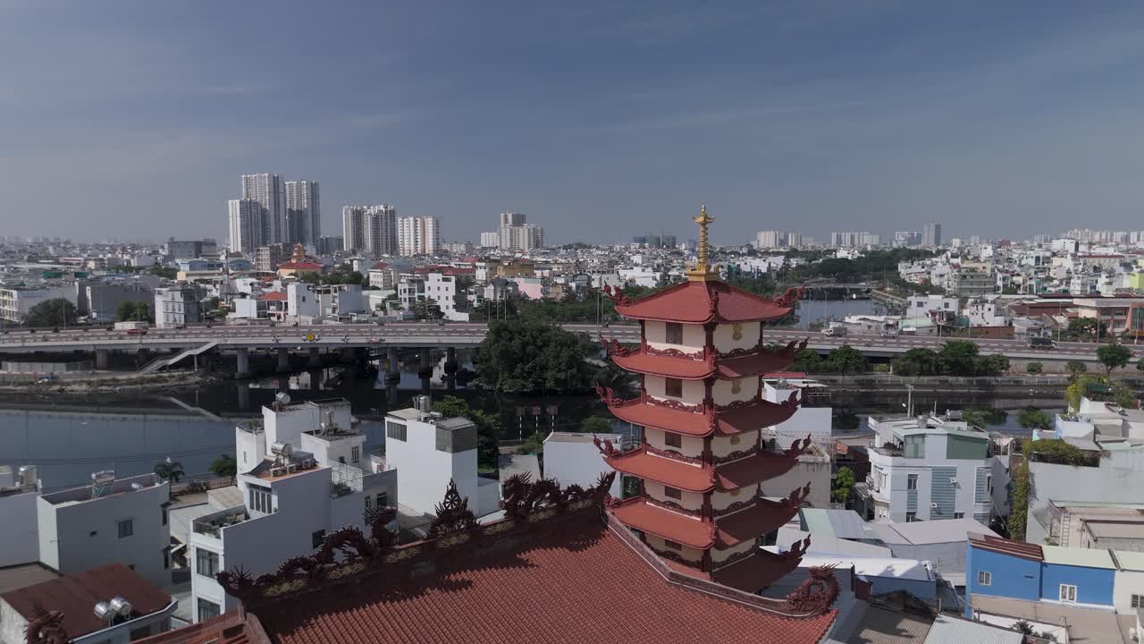Static drone view of Buddhist pagoda in busy urban area of Ho Chi Minh City, Vietnam on a sunny clear day featuring transportation infrastructure of main roads and canals in background