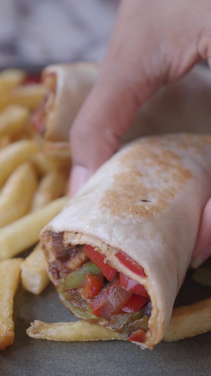 Une main saisissant un délicieux wrap fajita avec des frites