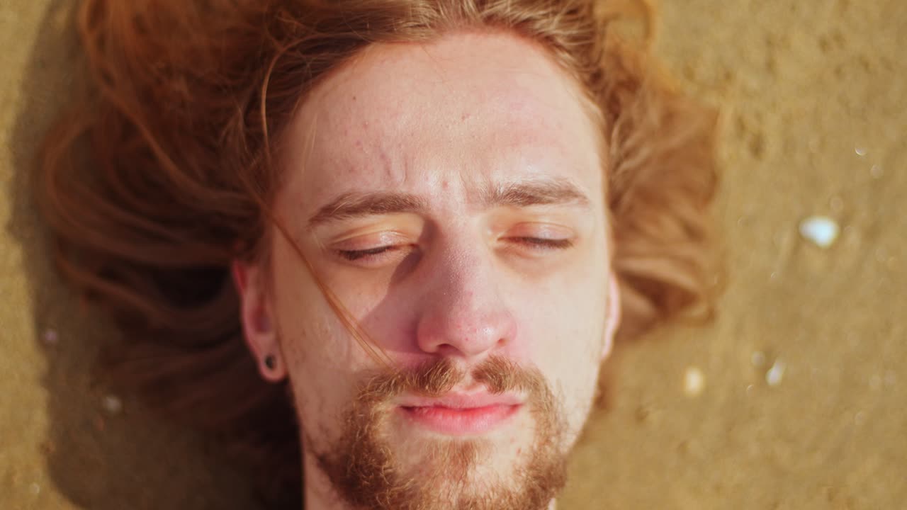 A Scene of a Man Waking Up on the Beach - Close Up