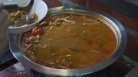 un primer plano de la mano de una chica tomando verduras cocidas y sopa en el buffet