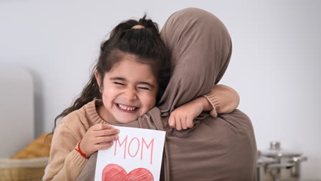 Daughter hugging her mother with a handmade Mother's Day card