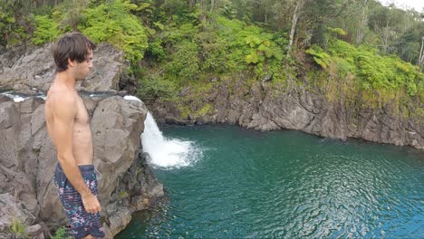 man jumps from a cliff into blue green water