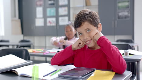 in school, boy in red smiling at desk in classroom
