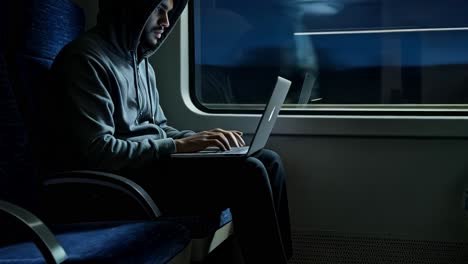 A man is deeply focused on his laptop while commuting on a train at night, completely immersed in the task at hand