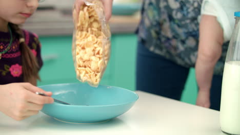 mother hands pouring corn flakes into blue bowl. preparing breakfast for child