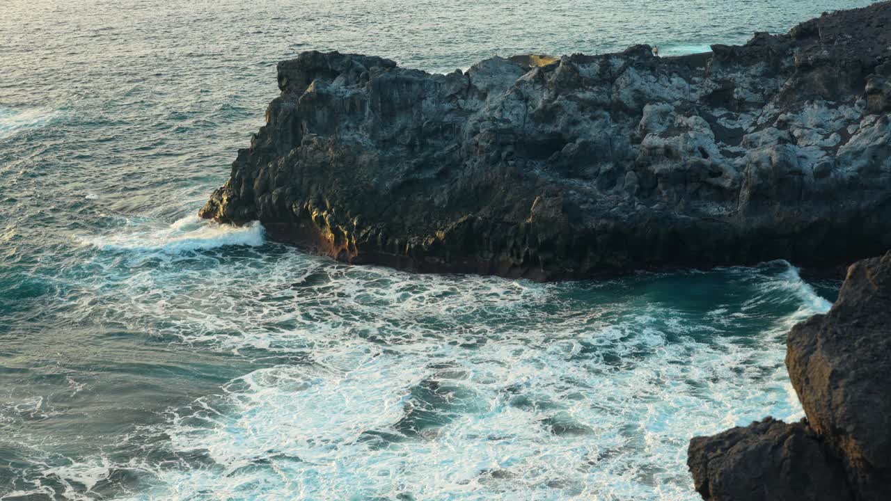 Onde dell'oceano si infrangono lungo la costa rocciosa al rallentatore mentre la luce dell'ora d'oro si diffonde sulle scogliere marine
