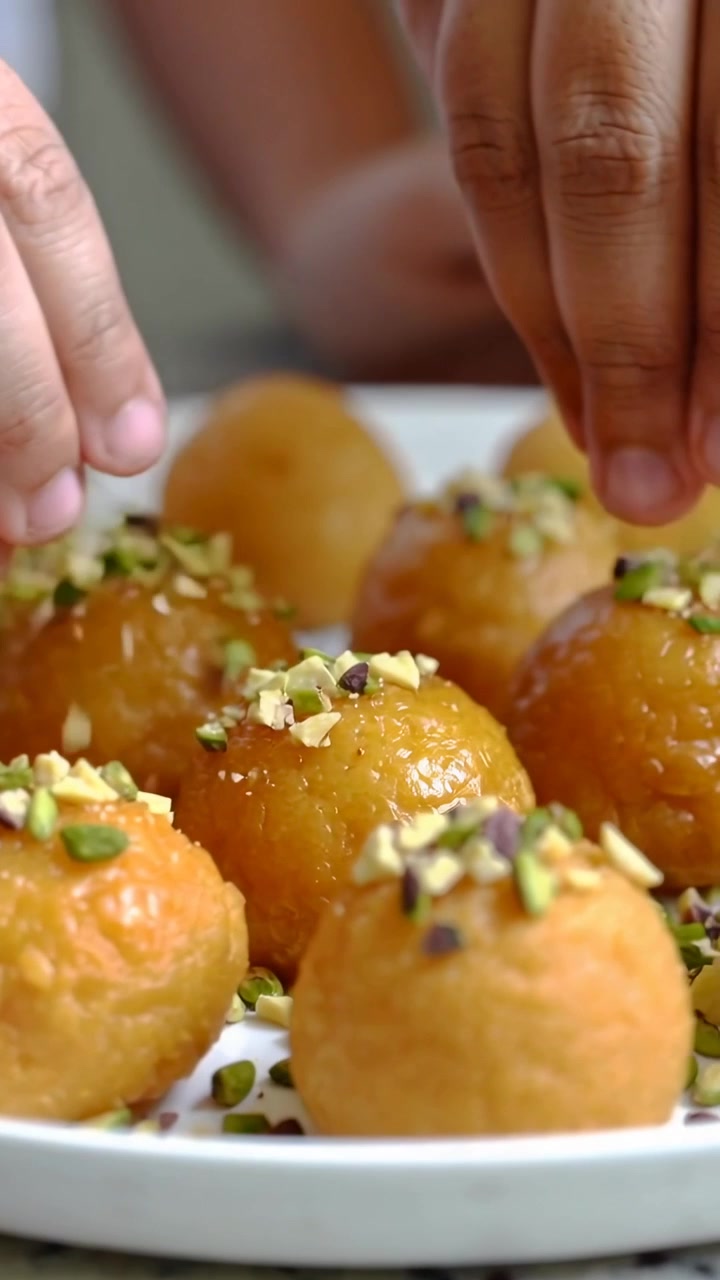 Video verticale: Mani che cospargono pistacchio su dolcetti a forma di pallina su un piatto, pronti per essere serviti al bancone.