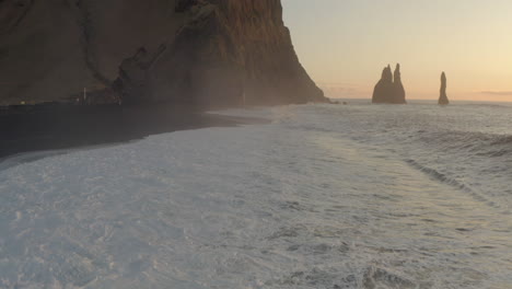 Toma-Aérea-Lenta-Sobre-La-Playa-De-Arena-Negra-Hacia-Columnes-Reynisfjara-Y-Pilas-De-Mar-Islandia