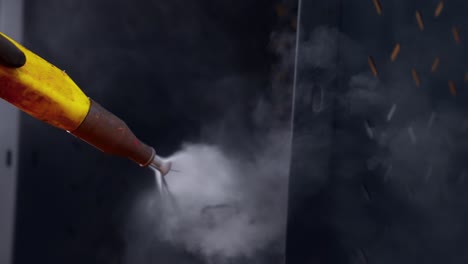 closeup of a person&#039;s hands wearing gloves inside a paint booth painting black metal plates with a powder paint gun in slow motion
