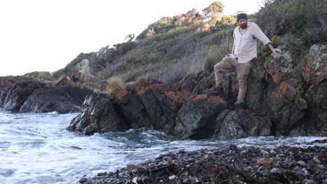 a fisherman waits on some coastal rocks for the high tide to scede so he can continue walking