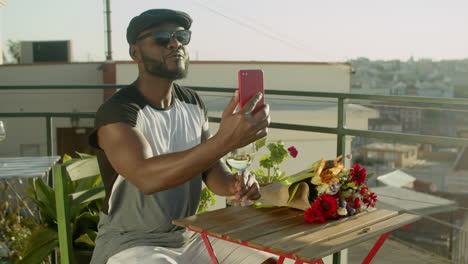 gay waiting for lover in rooftop cafe, having video conference