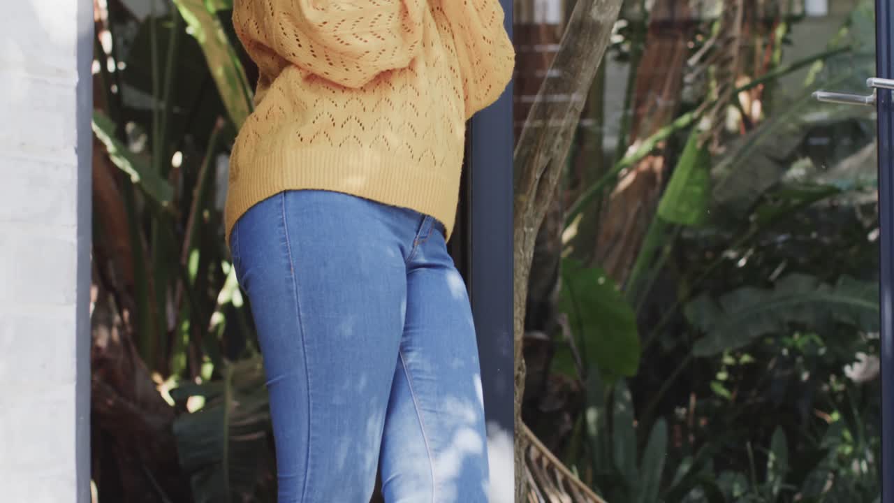 Happy biracial woman drinking coffee at window at home in slow motion