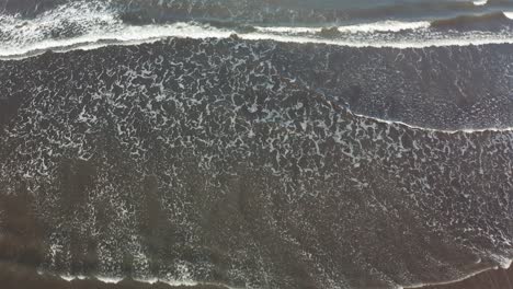 top down view of waves rolling over the beach - aerial drone shot