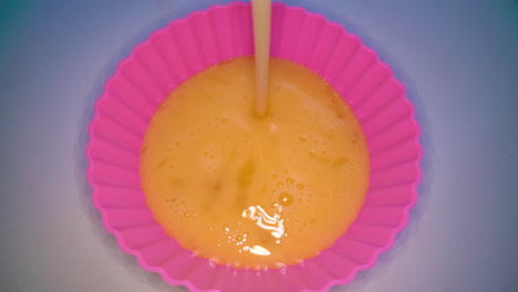 pouring beaten egg into pink baking form on white table