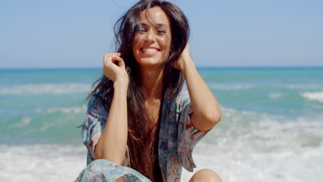 Mujer-Feliz-Sentada-En-La-Playa-Sosteniendo-Su-Cabello