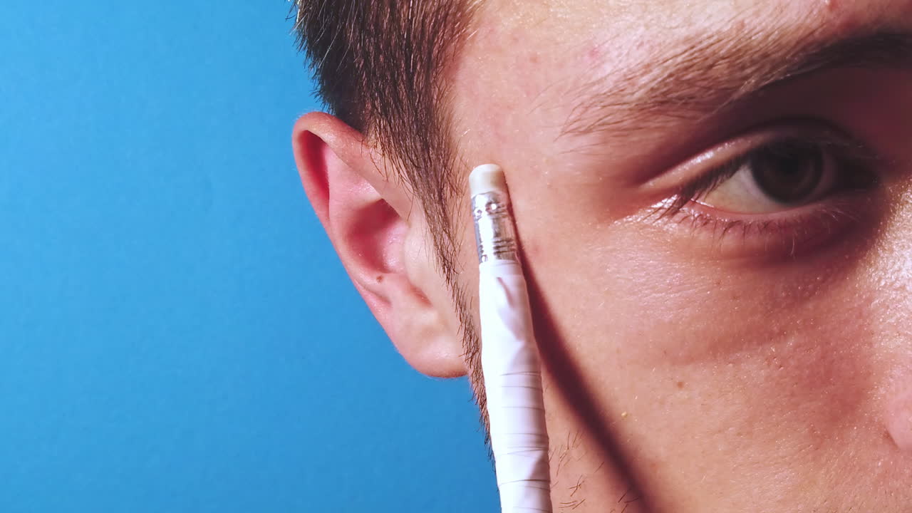 Close-up slow motion of thinking man with a pencil in front of a blue background