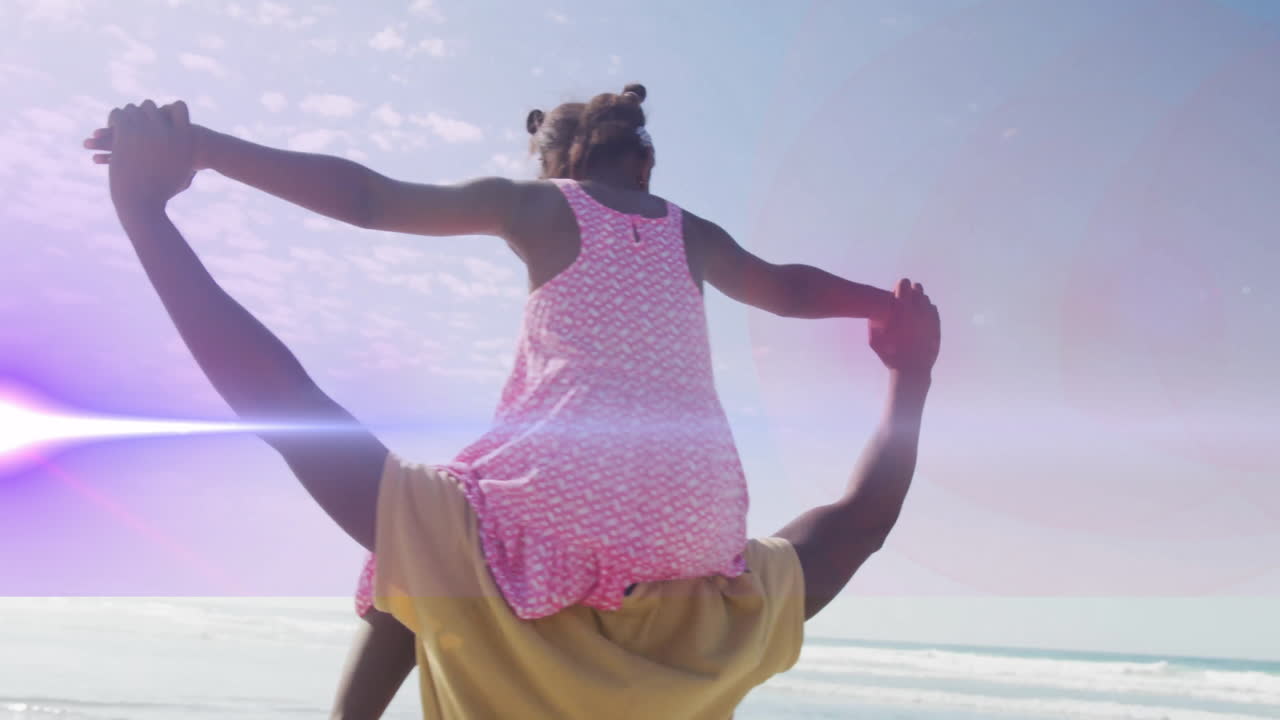 At beach, child in pink dress playing on adult's shoulders with animation