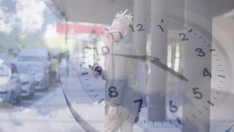 animation of clock over african american man using phone on street and moving cloudscape