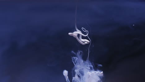 Slow-motion-video-of-white-watercolor-ink-mixing-in-water-against-blue-background