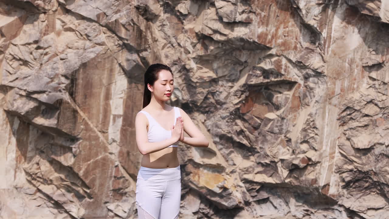 Casal jovem, calmo e espiritual, em roupas esportivas, em pé sobre uma rocha em posição de lótus, praticando exercícios de yoga, respirando e meditando, fazendo o gesto namastê, com as pernas cruzadas e mantendo as mãos em mudra em um parque verde.
